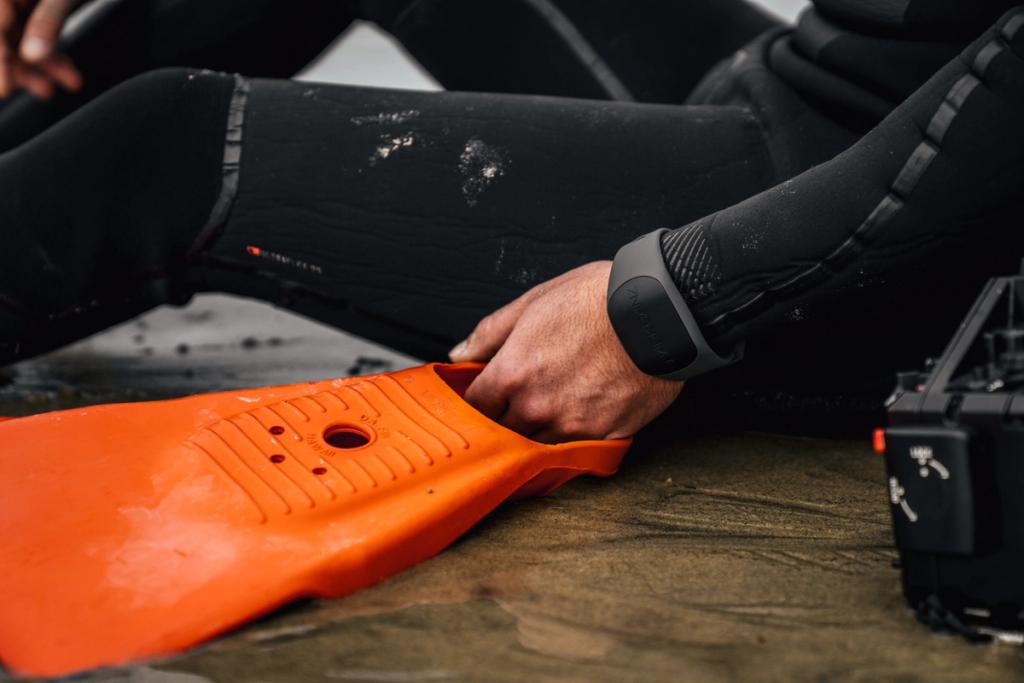 Diver in a wetsuit wearing a Sharkbanz band on the wrist while handling an orange fin