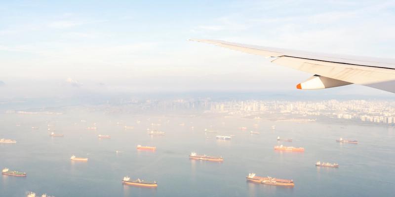 Aerial view from an airplane wing over a harbor crowded with anchored cargo ships near a city skyline
