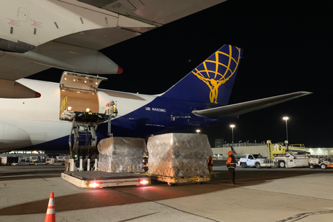 Workers load shrink-wrapped cargo pallets into a purple freighter aircraft on a tarmac at night