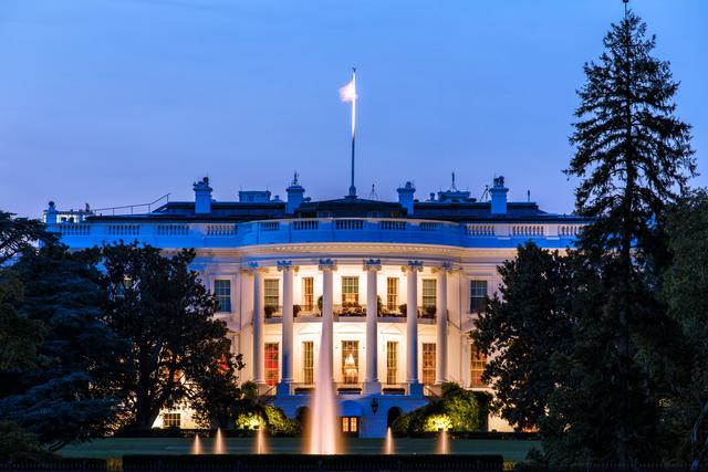 The White House South Portico illuminated at dusk with fountains and an American flag flying above