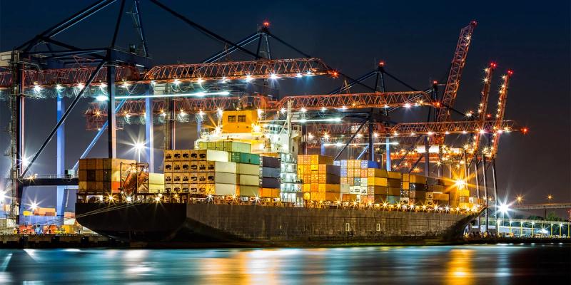 Container ship loaded with stacked containers berthed under illuminated gantry cranes at a port at night