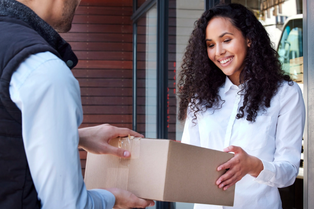 Woman receiving a cardboard box from man at doorway while smiling.