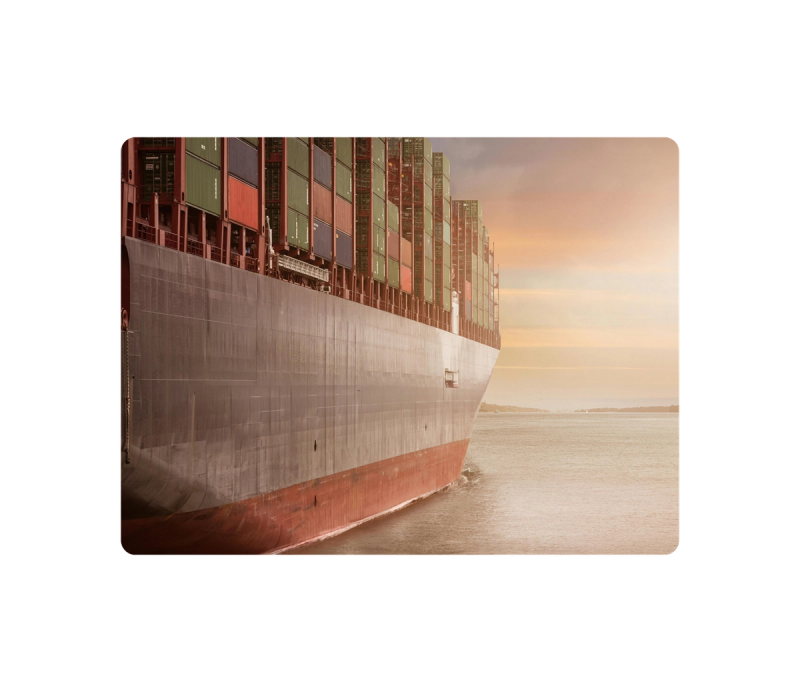 Container ship bow loaded with stacked containers gliding through open water at sunset