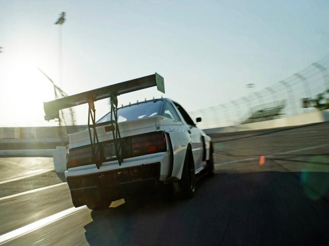 White race car with a large rear wing speeds down a track at sunset