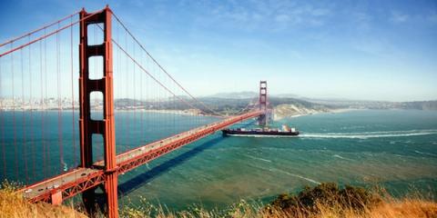 Golden Gate Bridge spanning San Francisco Bay with a container ship passing beneath on a clear day.