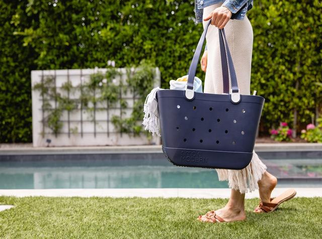 Woman carrying a navy Simple Modern rubber tote bag while walking beside a backyard pool