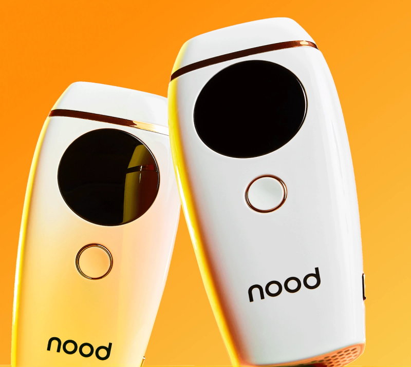 Close-up of two white Nood IPL hair removal devices against an orange gradient background