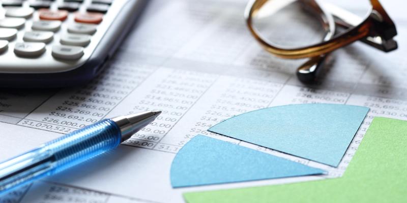 Blue ballpoint pen, calculator, paper pie chart and glasses resting on a financial spreadsheet