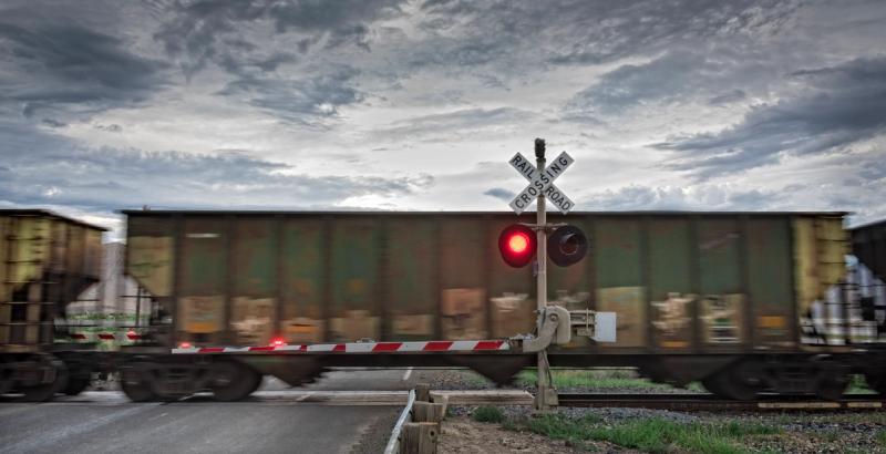 Freight train moving past a railroad crossing sign and red signal light beneath a dramatic cloudy sky