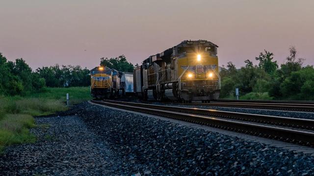 Union Pacific freight train with locomotives on railroad tracks at dusk, headlights on, beside a parallel track