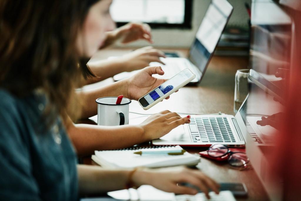 People working on laptops and a smartphone at a shared office table