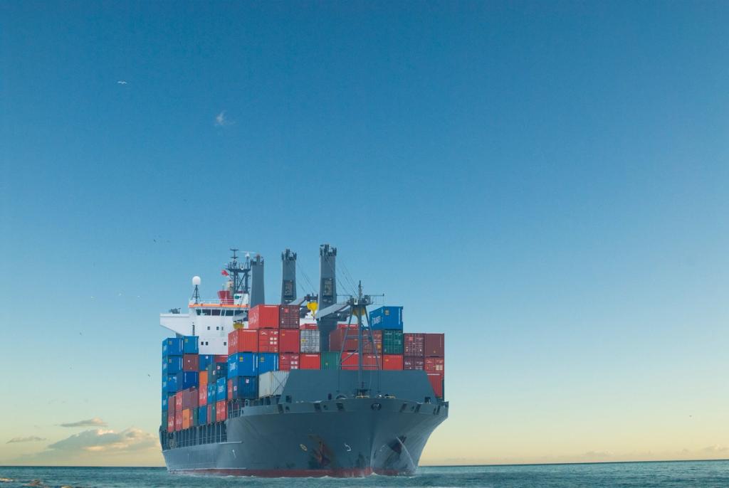 Aerial view of a container terminal at sunset with rows of stacked containers, gantry cranes and trucks on the quay