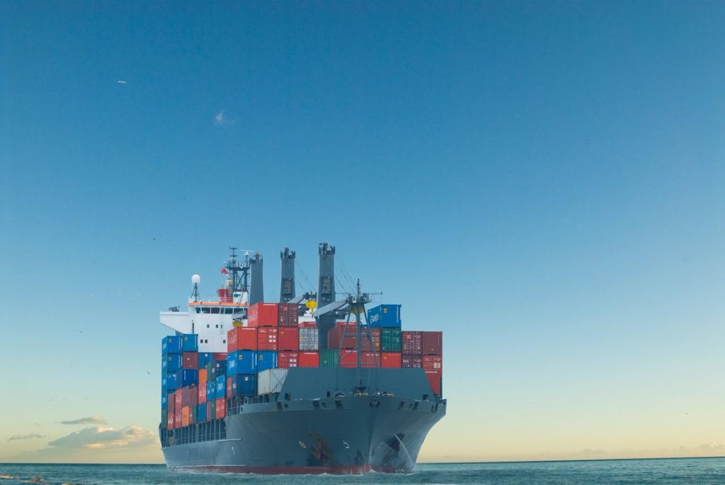 Aerial view of a container terminal at sunset with rows of stacked containers, gantry cranes and trucks on the quay