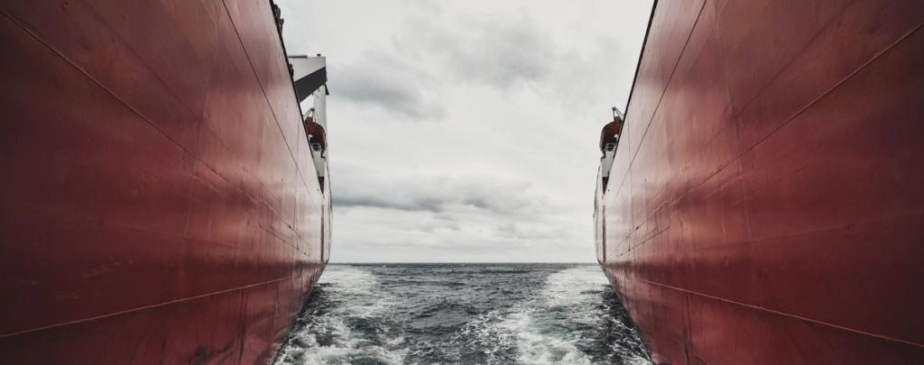 View between the towering red hulls of two ships, churning sea and grey horizon visible in the gap.