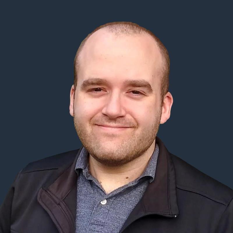 Headshot of a smiling man with a beard in a dark jacket over a grey polo shirt