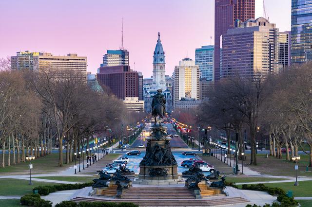 Philadelphia skyline at dusk with City Hall and the Washington Monument on the Parkway in the foreground.