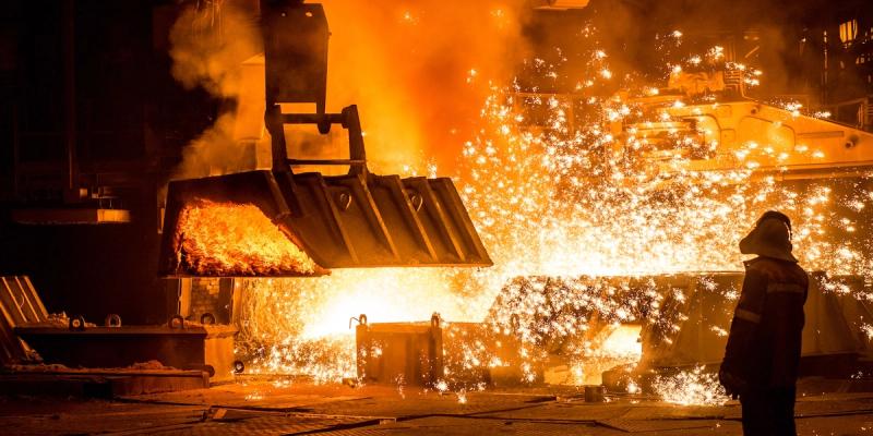 Worker silhouetted against molten metal and flying sparks pouring inside a steel mill