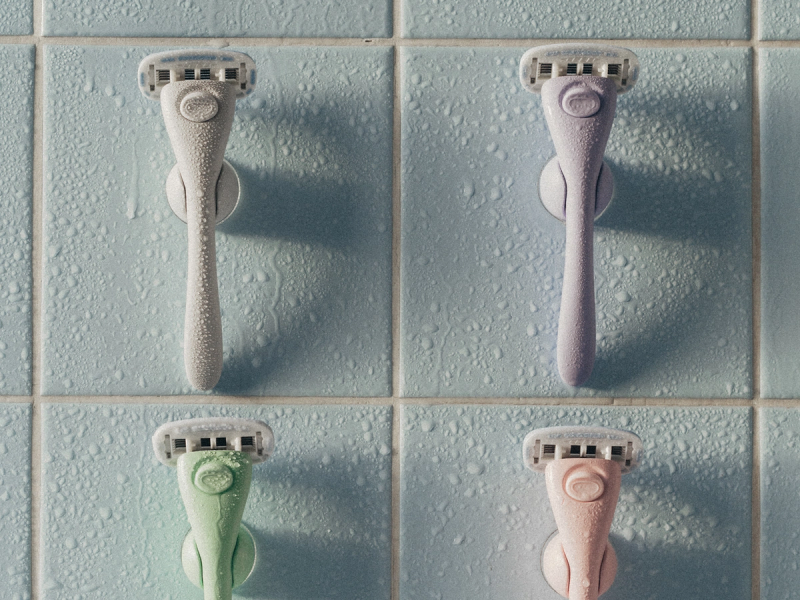 Four pastel-colored Estrid razors mounted on suction holders on blue shower tiles