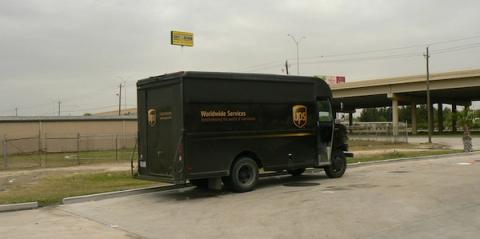 Brown UPS Worldwide Services delivery truck turning in a paved lot beside a highway overpass