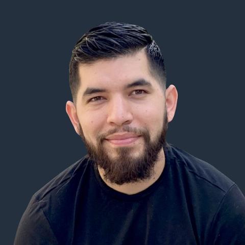 Headshot of a smiling bearded man in a black T-shirt against a dark blue background