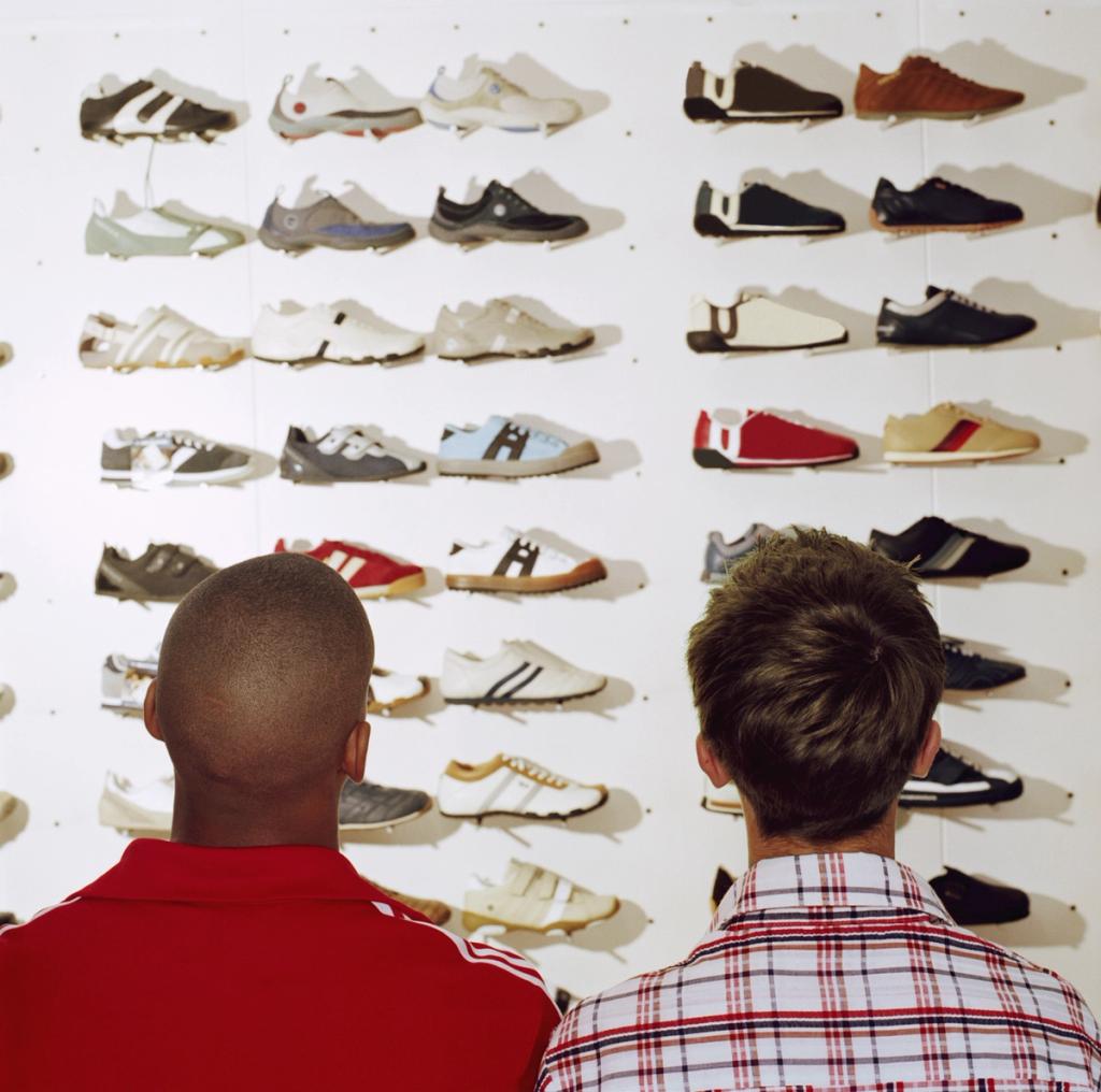 Two shoppers browsing a wall display of sneakers and athletic shoes in a store