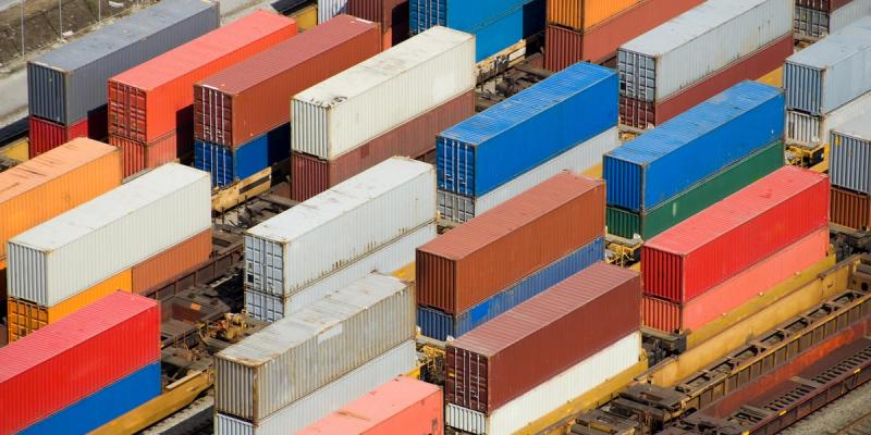 Aerial view of rows of stacked red, blue, and white shipping containers on rail cars