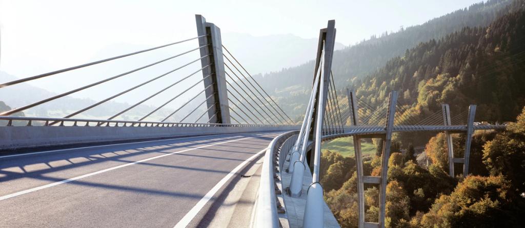 Cable-stayed concrete highway bridge curving through a forested mountain valley