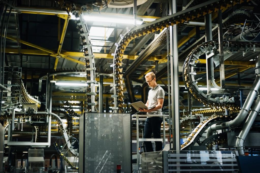 Worker with a laptop on a walkway amid yellow overhead conveyor lines in an industrial manufacturing plant