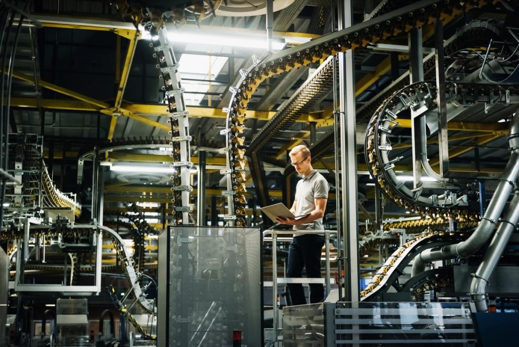 Worker with a laptop on a walkway amid yellow overhead conveyor lines in an industrial manufacturing plant