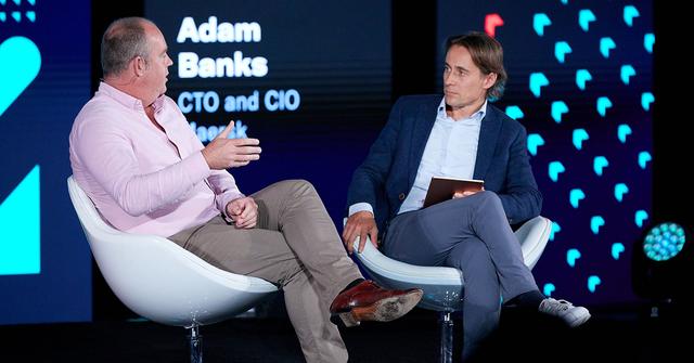 Two men in chairs on a conference stage; screen labels Adam Banks, CTO and CIO of Maersk