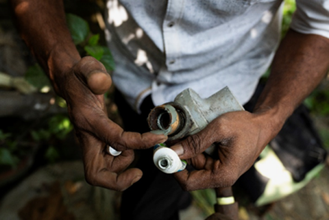 A worker's hands holding a metal gas pipe fitting during a methane leak repair