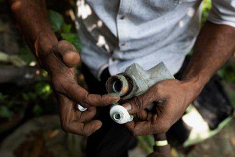 A worker's hands holding a metal gas pipe fitting during a methane leak repair