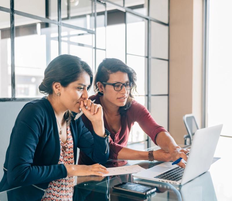 Two colleagues reviewing paperwork together at a laptop in a bright office