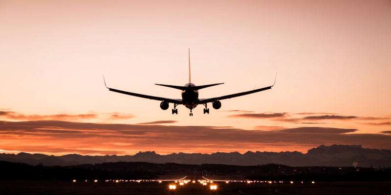 Silhouette of a passenger jet landing on a runway at sunset with mountains and runway lights