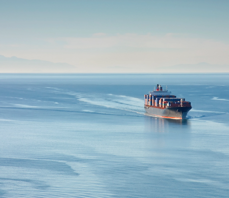 Container ship sailing across calm open ocean under a hazy sky