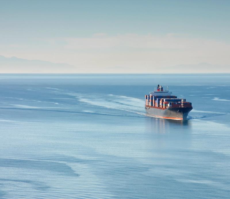Container ship sailing across calm open ocean under a hazy sky