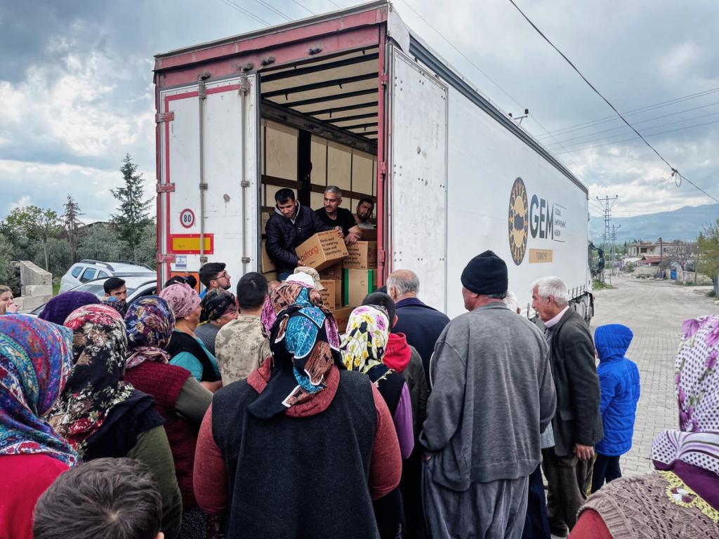 People gathered at the back of a GEM box truck as men unload cartons of aid supplies