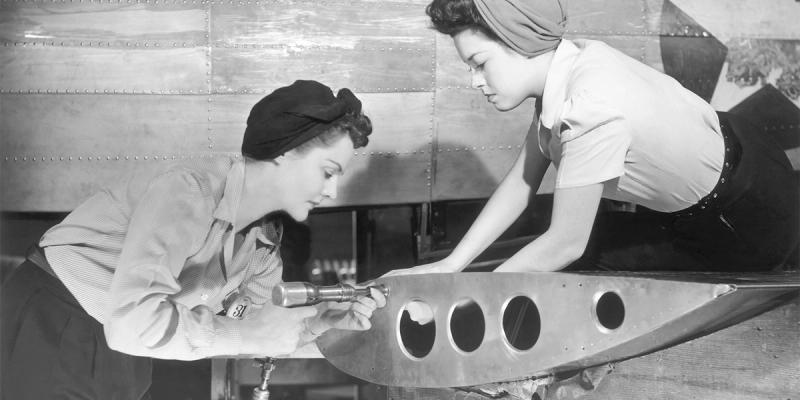 Vintage black-and-white photo of two women assembling a riveted aircraft part in a factory