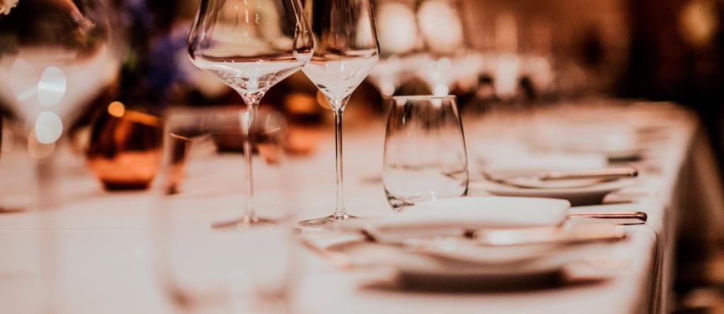 Close-up of wine glasses and place settings on a long white-clothed restaurant table