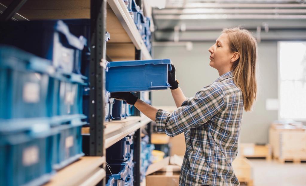 Worker lifting a blue tote from a storage rack in a warehouse aisle