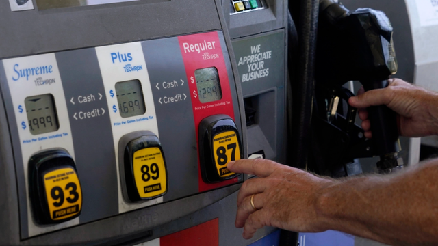 Close-up of a gas station fuel pump showing octane buttons for Supreme 93, Plus 89 and Regular 87 as a hand reaches for it
