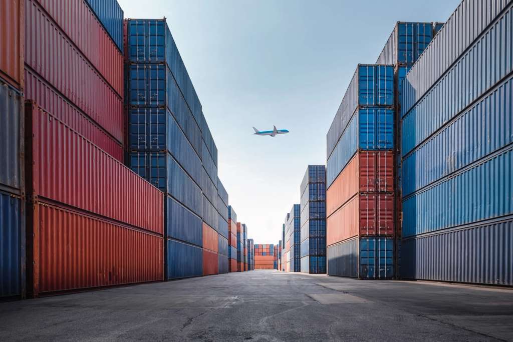 Rows of stacked shipping containers line a cargo terminal corridor.