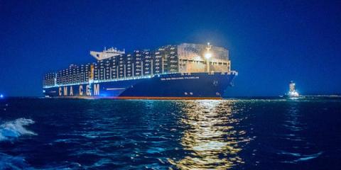 Illuminated CMA CGM container ship sailing on water at night with a tugboat alongside