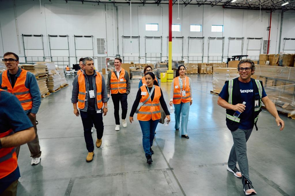 Group in orange safety vests walking through a warehouse, a man in Flexport vest leading