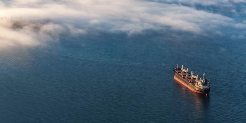 Aerial view of a bulk cargo ship anchored alone on calm blue water under low fog