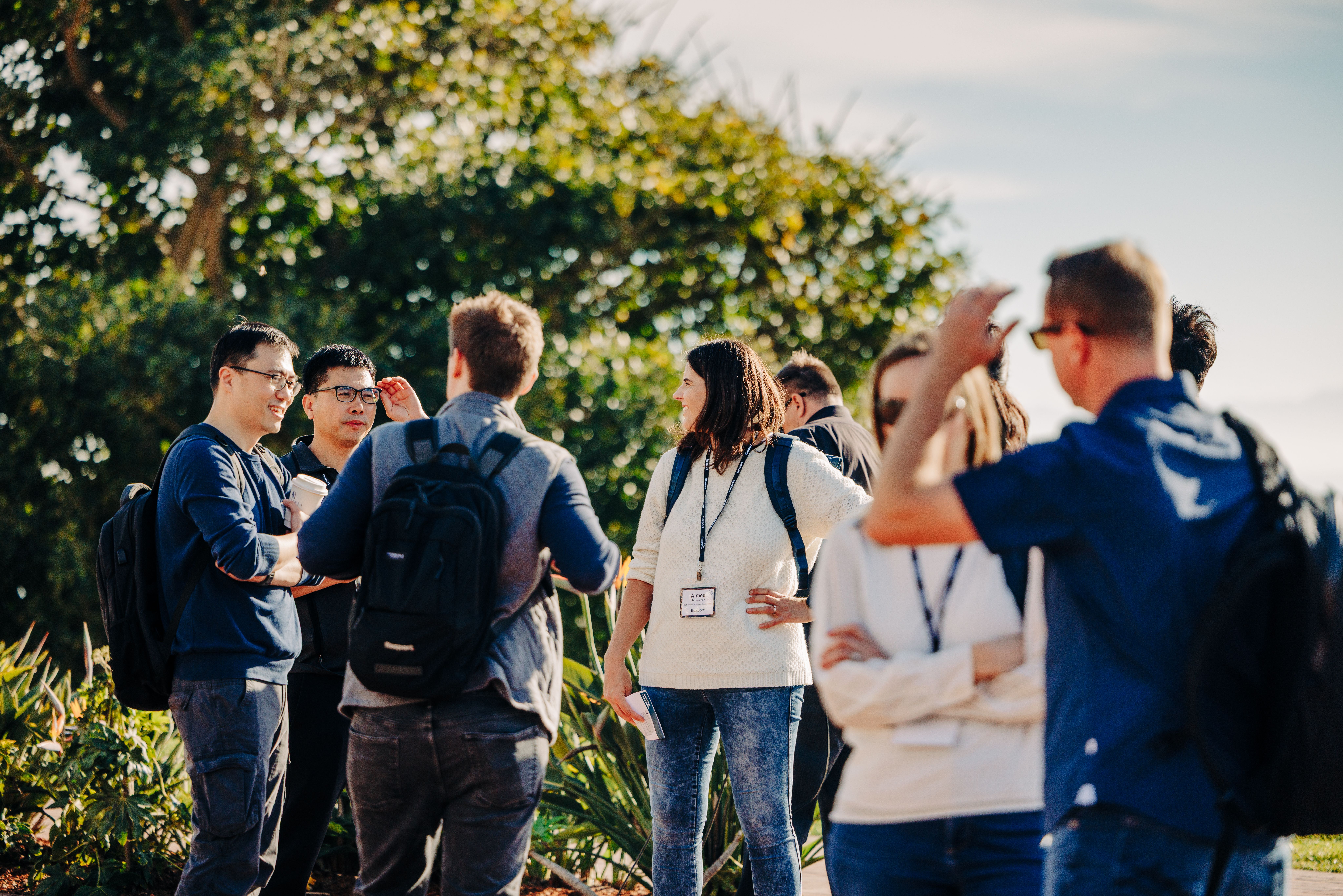 A group of people wearing ID badges gather outdoors for a discussion or educational event.