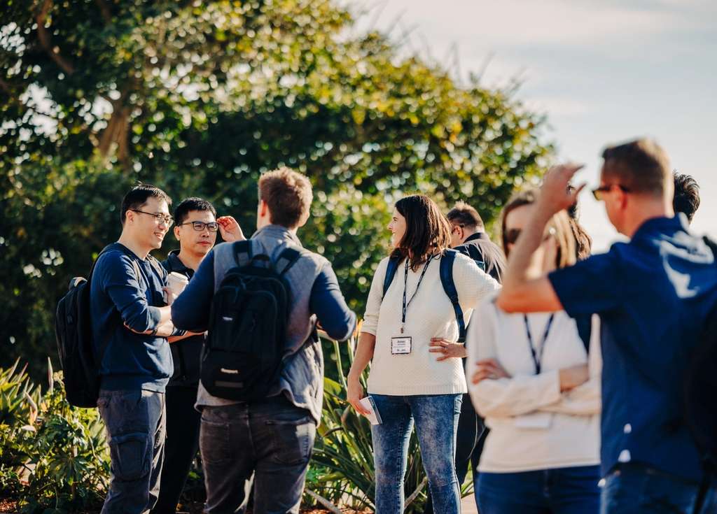 A group of people wearing ID badges gather outdoors for a discussion or educational event.