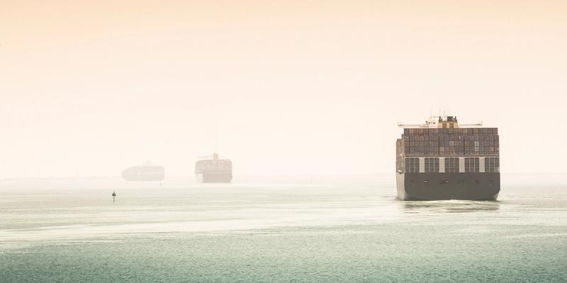 Container ships at sea in hazy light, one large vessel approaching the foreground