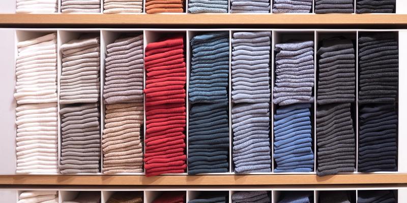 Retail shelves of neatly folded knit sweaters sorted by color, with one column in bright red