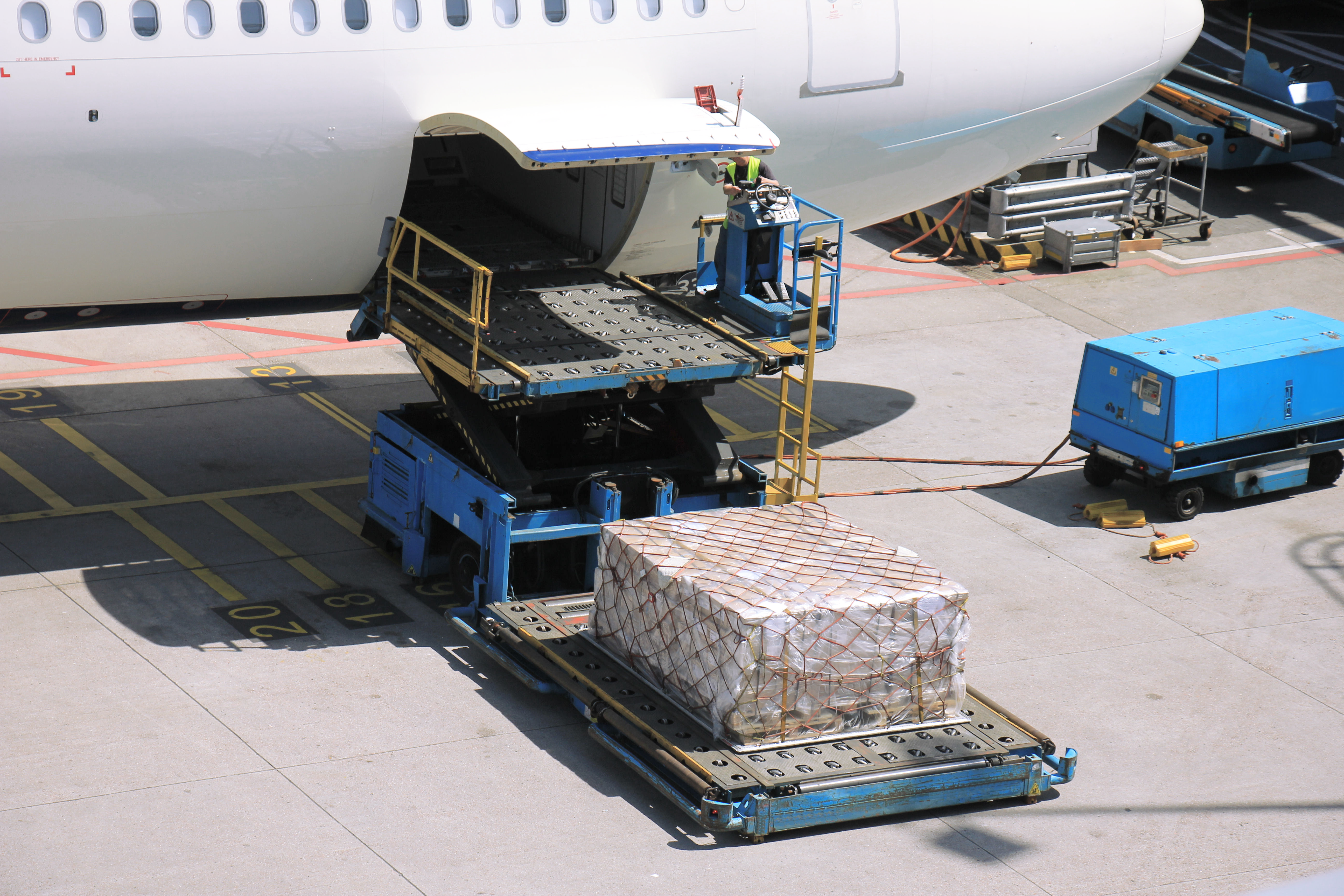 Ground crew loads cargo onto an aircraft using an air cargo loader.